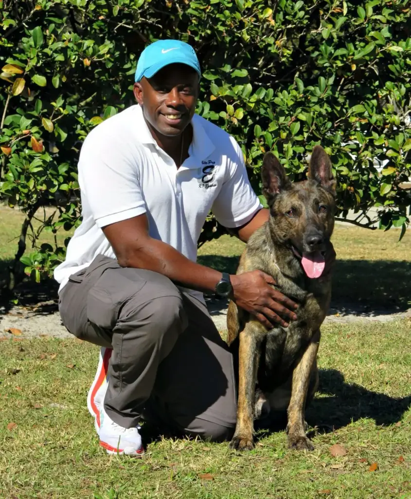Laurent Gabriel smiling, kneeling beside a dog in front of a hedge